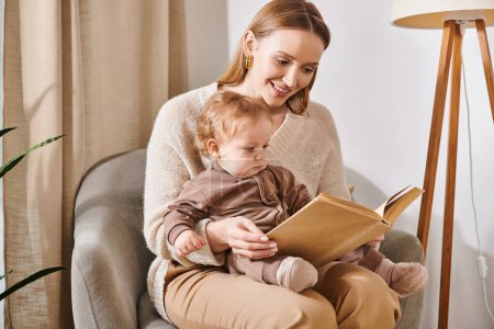 happy mother reading book to adorable toddler son in armchair in cozy nursery room, modern parenting
