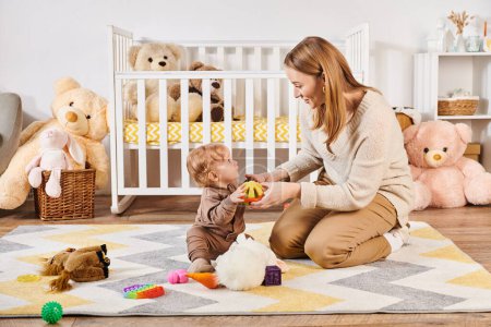 happy mother and toddler child playing with soft toys near crib in nursery room, modern parenting