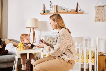 junge Mutter füttert kleinen Sohn mit Frühstück auf Kinderstuhl im Kinderzimmer, moderne Kindererziehung
