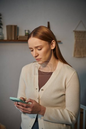Foto de Frustrado y molesto mensajería mujer joven en el teléfono móvil en cuarto oscuro de la guardería en casa - Imagen libre de derechos
