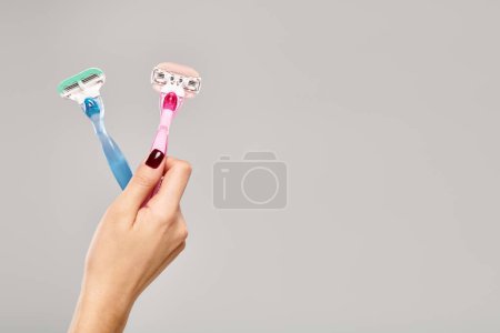 object photo of pink and blue razors in hand of unknown woman with nail polish on gray background