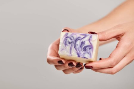 object photo of striped bar of soap in hands of unknown female with nail polish on gray backdrop