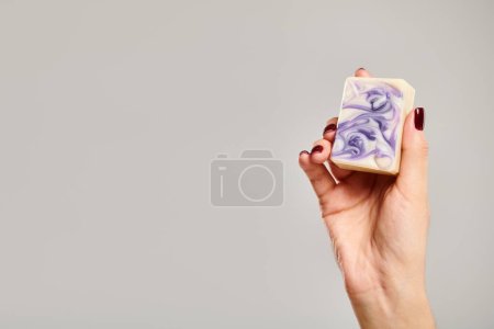 unknown young female model with nail polish holding bar of striped soap on gray background