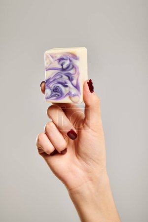 object photo of bar of purple striped soap in hand of unknown woman posing on gray background