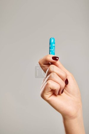 object photo of hygienic tampon in hand of unknown woman with nail polish on gray background