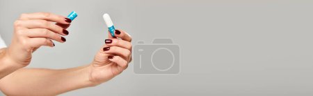 hygienic tampon in hands of unknown young female model on gray backdrop, object photo, banner