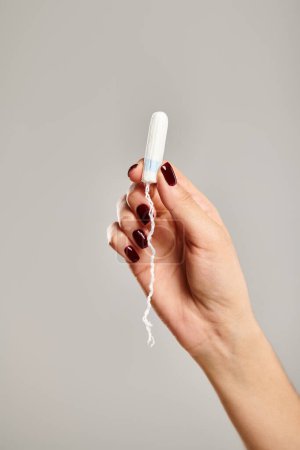 Foto de Modelo femenino joven desconocido con esmalte de uñas sosteniendo en la mano tampón higiénico sobre fondo gris - Imagen libre de derechos