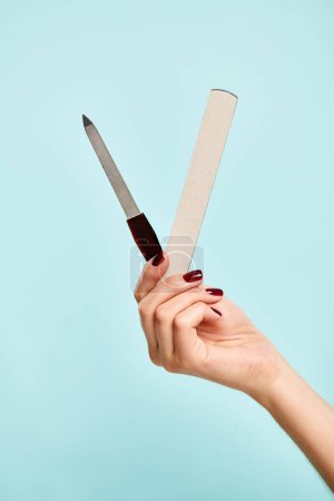 two nail files in hand of unknown young  woman with nail polish on blue backdrop, object photo