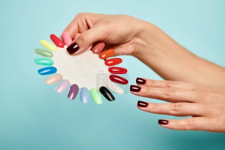 young unknown woman holding nail polish palette in hands on vibrant blue background, object photo