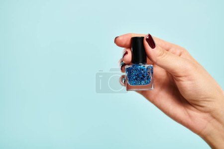 object photo of blue vibrant nail polish in hand of young unknown woman of blue background