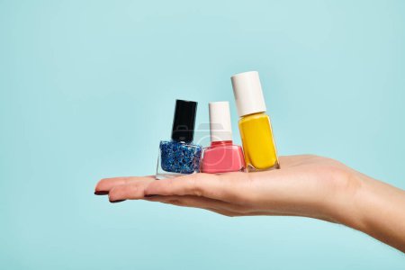 young unknown female model holding blue pink and yellow nail polish on her hand on blue backdrop