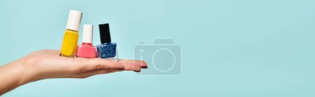 young unknown woman holding blue pink and yellow nail polish on her hand on blue backdrop, banner