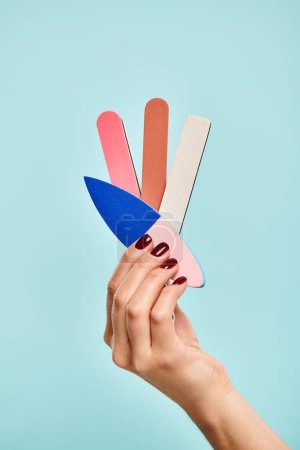 Foto de Objeto foto de diferentes limas de uñas en la mano de la joven mujer desconocida con esmalte de uñas sobre fondo azul - Imagen libre de derechos