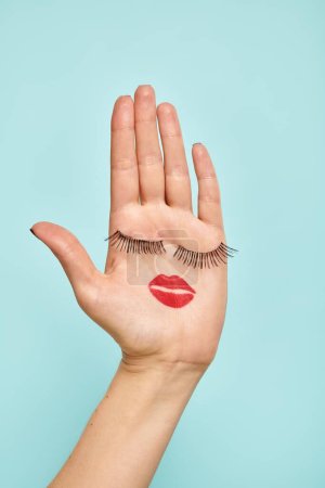 black artificial eyelashes and lipstick on palm of young unknown woman on vibrant blue background