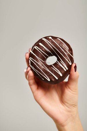 object photo of gourmet donut with brown icing in hand of unknown woman on gray background
