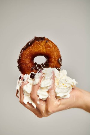 object photo of delicious donut with brown icing and whipped cream in hand of young unknown woman