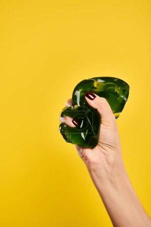 unbekannte junge weibliche Modell quetscht köstliche grüne Jello auf lebendigen gelben Hintergrund