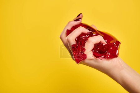 unknown female model squeezing red delicious jello in her hand on vibrant yellow background