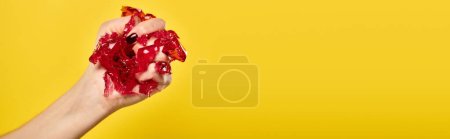 unknown woman with nail polish squeezing red jello in her hand on vibrant yellow backdrop, banner