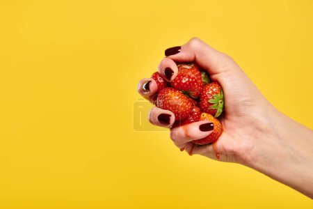 Unbekanntes weibliches Modell drückt saftige leckere Erdbeeren in der Hand auf gelbem Hintergrund