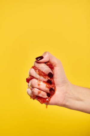 unknown young female model squeezing red juicy strawberries in her hand on yellow background
