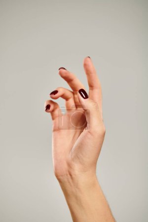 mano con esmalte de uñas oscuro de modelo femenino joven desconocido apuntando hacia arriba mientras sobre fondo gris