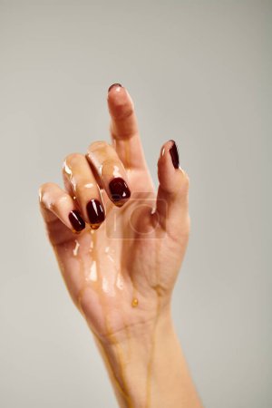 hand of unknown female model with nail polish covered with pure golden honey on gray background