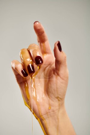 Hand einer unbekannten Dame zeigt nach oben, während sie mit Bio-Honig vor grauem Hintergrund bedeckt ist