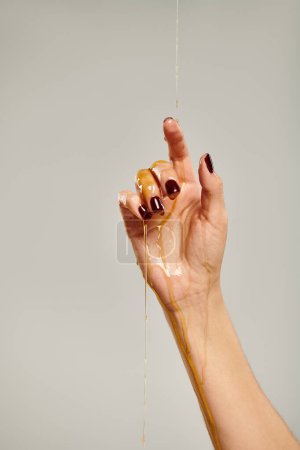 Hand von unbekannten jungen weiblichen Modell mit natürlichen köstlichen Honig auf grauem Hintergrund bedeckt