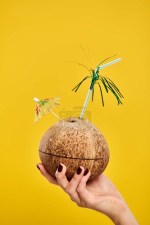 object photo of cocktail in fresh coconut decorated with umbrella in hand of unknown woman