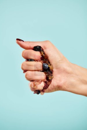 unknown young woman with nail polish squeezing fresh juicy blueberries in her hand on blue backdrop