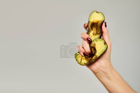 unknown woman with nail polish squeezing gourmet healthy avocado in her hand on gray background