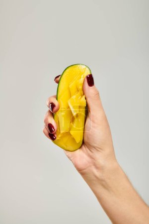 unbekannte junge weibliche Modell drückt saftige süße Mango in der Hand, während auf grauem Hintergrund