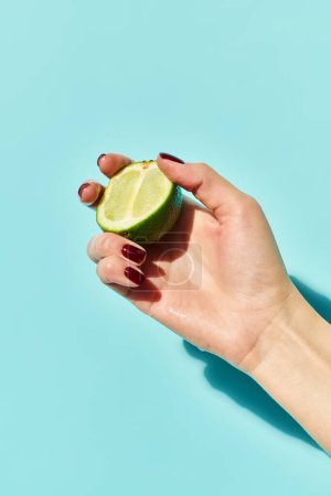 citron vert frais juteux à la main d'une femme inconnue avec vernis à ongles posant avec elle sur fond bleu