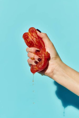 rote saftige leckere Tomatenstücke, gepresst von unbekannten weiblichen Modell auf lebendigem blauen Hintergrund