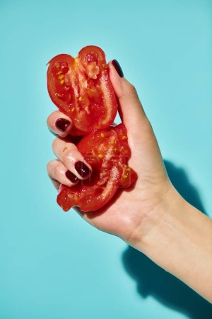 red delicious gourmet pieces of fresh tomato squeezed by unknown female model on vivid background