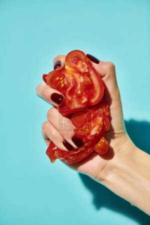Unbekannte Frau presst zwei Teile roter frischer köstlicher Tomaten auf leuchtend blauem Hintergrund