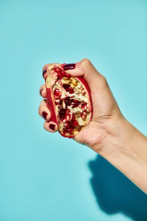 unknown female model squeezing delicious pomegranate on blue vibrant background, object photo