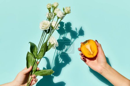 object photo of fresh eustoma and persimmon in hands of female model on blue vibrant background