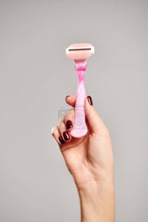unknown female model with nail polish holding pink razor in hand posing on gray background