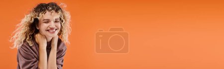 Téléchargez les photos : Femme avec les cheveux ondulés en couleur moka élégant col roulé souriant avec les yeux fermés sur l'orange, bannière - en image libre de droit