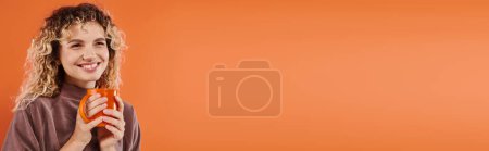 Téléchargez les photos : Femme heureuse avec les cheveux bouclés et tasse de café du matin regardant loin sur orange, bannière horizontale - en image libre de droit