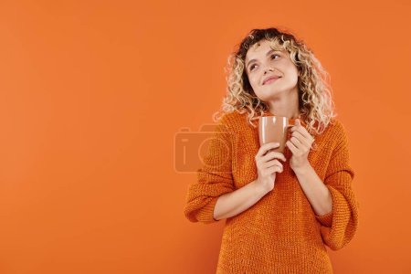 dreamy and positive curly hair with cup of morning coffee looking away on vibrant orange backdrop