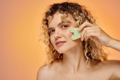 happy curly woman with perfect skin using gua sha looking at camera on pastel gradient backdrop puzzle #696258796