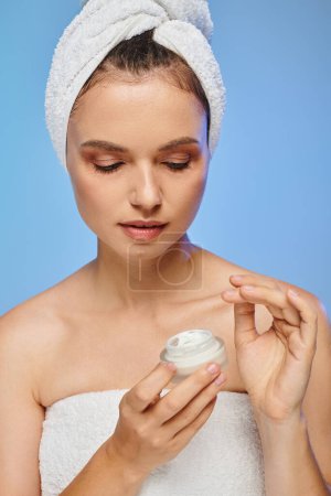 mesmerizing woman with towel on head holding container with cosmetic face cream on blue backdrop Stickers 696259964