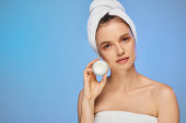 alluring woman with towel on head showing jar of face cream on blue backdrop, wellness and beauty magic mug #696260042