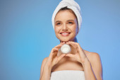 smiling model with towel on head holding jar of face cream on blue backdrop, wellness and beauty Stickers #696260254