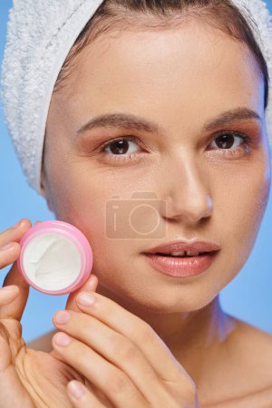 portrait rapproché de femme avec visage parfait et serviette sur la tête avec pot de crème cosmétique sur bleu