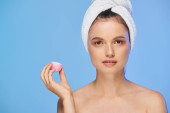attractive woman with glowing skin and towel holding cosmetic cream and looking at camera on blue mug #696260410