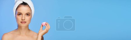 Photo for Charming woman with glowing skin and towel holding cosmetic cream looking at camera on blue, banner - Royalty Free Image